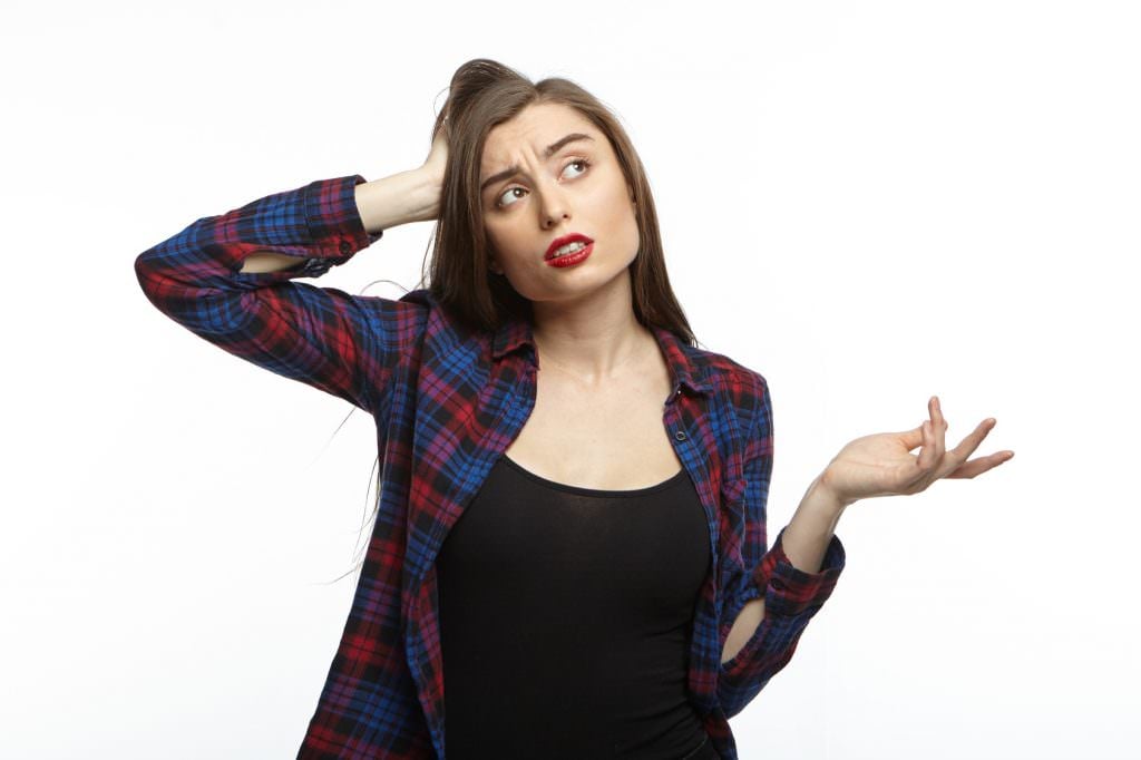 Isolated shot of attractive brunette young female wearing red lipstick shrugging her shoulders and making uncertain gesture, having some doubts, feeling confused while making some decisions