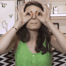 Nathalia Arcuri de blusa verde, com o dedo polegar e o indicador juntos e na frente dos olhos, como se imitasse binóculos